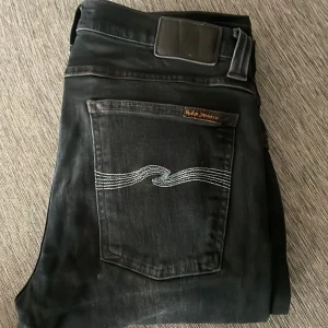  Nudie Jeans, W32 L34 (prisförslag) - Svarta jeans från Nudie Jeans med klassisk vågstickning på bakfickan. Jeansen har en rak passform och är tillverkade i mjuk bomull med en lätt tvättad look. Perfekta för dig som gillar stilrena och bekväma jeans med snygga detaljer.