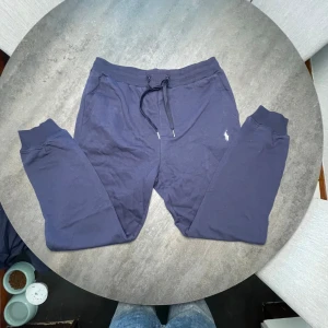 Mörkblå mjukisbyxor Polo Ralph Lauren - Köpte fel storlekMörkblå mjukisbyxor från Polo Ralph Lauren med klassisk broderad logga på benet. Byxorna har snörning i midjan, ribbade muddar vid bensluten och en bakficka med dragkedja. Tillverkade i mjuk bomull för maximal komfort.