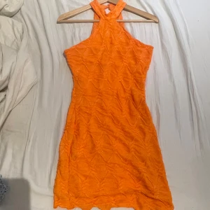 Orange kort klänning med struktur - Superfin orange kort klänning från Gina tricot med strukturerat tyg och glittriga detaljer. Klänningen har halterneck och är ärmlös med figurnära passform. Perfekt för dig som vill sticka ut med färg och cool textur.
