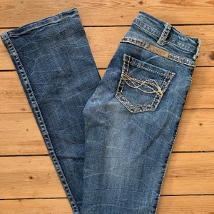 Blå jeans från Tuff Co. med broderi W28 L32 - Snygga blå jeans från Tuff Co. med kontrasterande grova sömmar och broderi på bakfickan. Klassisk femficksmodell med raka ben och coola detaljer längs fickor och midja. Perfekta för dig som gillar en unik och avslappnad stil.   Storlek W28 L32