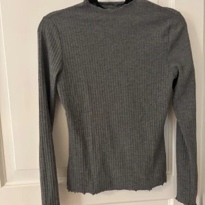 Grå ribbad långärmad tröja ONLY - Grå långärmad tröja från ONLY i ribbat material. Tröjan har en tight passform, rund halsringning och vågig kant nertill och vid ärmslut. Använd fåtal gånger 