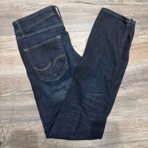 Mörkblå slim jeans Jack & Jones - Snygga mörkblå jeans från Jack & Jones, modell Slim/Glenn. Jeansen har klassisk femficksdesign, gul kontrastsöm och lätt slitna detaljer framtill.