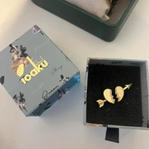 Ring från ioaku - Snygg ring från Ioaku i guldtonad metall, formad som ett trasigt hjärta med en pil genom. Ena halvan av hjärtat är dekorerad med små glittrande stenar. Har vart slutsåld länge 