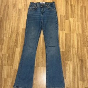 Blå bootcut jeans från Zara, stl 34 - Snygga lowaisted blåa jeans från Zara i klassisk bootcut-modell. Jeansen har fem fickor, normal passform och är tillverkade i ett mjukt bomullstyg med lätt stretch. Perfekt för dig som gillar en tidlös look med lite utsvängda ben.