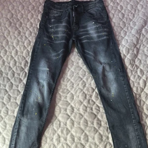 Svarta skinny jeans från Dsquared2 - Snygga svarta skinny jeans från Dsquared2 med coola slitningar och färgstänk i gult och vitt. Jeansen har klassisk femficksdesign, Dsquared2-logga vid gylfen och en gul ICON-lapp bak. Tillverkade i Italien i stretchig bomull för skön passform.