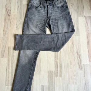 Grå slim fit jeans Jack & Jones W30 L30 - Snygga grå jeans från Jack & Jones i modellen Slim/Glenn. Jeansen har en smal passform, klassisk femficksdesign och är tillverkade i mjukt denimtyg. Perfekta för dig som gillar en stilren look med lite tvättad känsla.