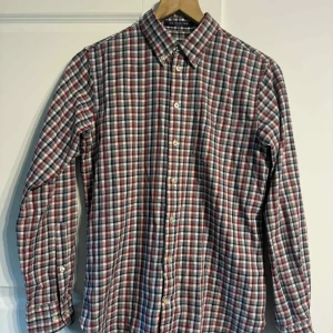 Rutig skjorta från GANT i bomull - Riktigt snygg rutig skjorta från GANT i bomull. Skjortan har klassisk krage, knappar hela vägen och broderad logga på bröstet. Färgerna är röd, blå, grå och vit. Perfekt för dig som gillar en avslappnad men stilren look. XS~164 (13-14y)