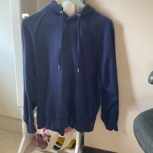 Mörkblå hoodie från H&M Divided - Mörkblå hoodie från H&M Divided med klassisk känguruficka och snörning i huvan. Mjuk insida och ribbade muddar vid ärmslut och nederkant. Perfekt för chill dagar eller när du vill ha något bekvämt och stilrent.