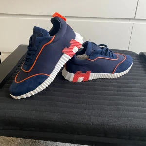 skor - Snygga sneakers i marinblå mocka och textil med orange detaljer och vit, räfflad sula. Skorna har coola orange inslag på sulan och en modern, sportig look. Perfekta för dig som vill sticka ut med exklusiva och trendiga sneakers. Låda medföljer tyvärr inte!