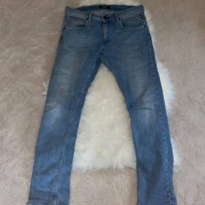 Blå Replay jeans, rak modell - Säljer ett par klassiska blå jeans från Replay med fem fickor och snygga detaljer vid fickan. Jeansen har rak passform och normal midja, tillverkade i mjukt denimtyg som är skönt att bära. Perfekta för dig som gillar stilrena och tidlösa jeans.