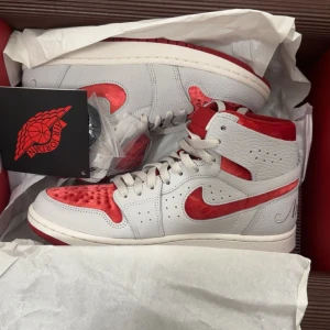 Nike Air Jordan 1 Retro röd/vit - Nike Air Jordan 1 Retro i en clean vit och röd färgkombination. Skorna har högt skaft, snörning och är tillverkade i skinn med röda detaljer i mocka. Ikonisk Swoosh-logga på sidan och klassisk Air Jordan branding. Perfekta för dig som vill sticka ut med stil.