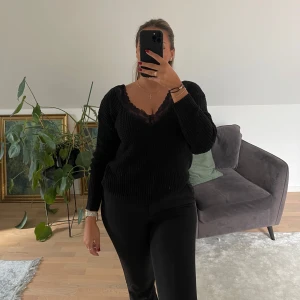 Svart stickad v-ringad tröja med spets - Svart stickad tröja med v-ringning och snygg spetskant framtill. Tröjan har lång ärm, ribbade muddar och en öppen detalj i ryggen. Perfekt för dig som gillar en lite mer dressad men ändå chill look.