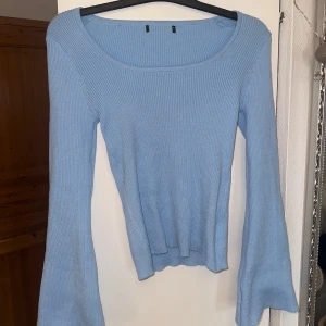 Ljusblå ribbad långärmad topp - Säljer en ljusblå ribbad topp med lång ärm och utsvängda ärmslut. Toppen har en rundad, bred urringning och är figurnära i modellen. 