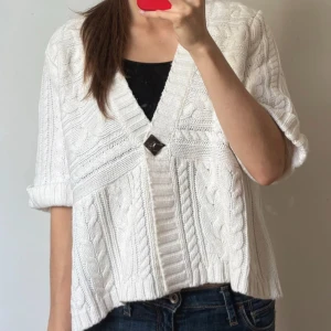Vit stickad kofta - Säljer en vit stickad kofta från Being Casual med korta ärmar och snygg kabelstickad design. Koftan har djup v-ringning och stängs med en dekorativ knapp framtill. Perfekt att slänga över ett linne eller t-shirt för en chill look.