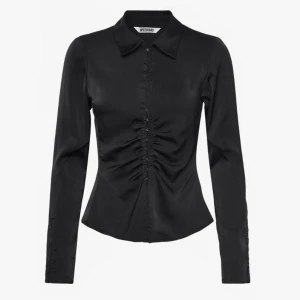 Figursydd satin skjorta - Oanvänd svart skjorta med lång ärm och figurnära passform. Klassisk krage och slät baksida. Perfekt för dig som gillar stilrena och trendiga plagg.