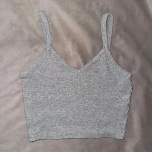 Glittrig croppad topp från Monki - Säljer en grå/glittrig croppad topp med smala axelband och v-ringning. Toppen är ribbad och har en tight passform som sitter snyggt på kroppen. Mycket fint skick!