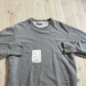 Grå sweatshirt från Acne Studios - Snygg grå sweatshirt från Acne Studios i mjuk bomull. Tröjan har rund halsringning, långa ärmar och diskret Acne Studios-logga tryckt nertill. Perfekt basic att ha i garderoben för en clean och stilren look.