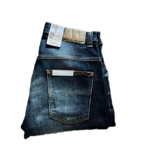 Nudie Jeans Thin Finn Indigo Dreams - Snygga blå jeans från Nudie Jeans, modellen Thin Finn Indigo Dreams. De har klassisk femficksdesign, orangea sömmar och en skinnpatch med logga bak. Jeansen är tillverkade i bomull och har en slim passform med raka ben. Perfekt för dig som gillar stilrena och tidlösa jeans.