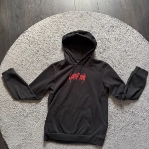 Svart hoodie med röd DECEPTION-print - Svart hoodie från Pier One med stor röd DECEPTION-print på bröstet och ryggen. Ryggen har även ett tryck med läppar och text i rött. Klassisk känguruficka och huva. Perfekt för dig som gillar streetwear och vill sticka ut.