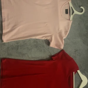 Två tighta t-shirts i rött och ljusrosa - Säljer två stilrena t-shirts i tight passform. En röd från Tommy Hilfiger med liten logga på bröstet och en ljusrosa från Gina Tricot. Båda har rund halsringning och korta ärmar. Perfekta för en clean och enkel look.