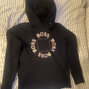 Hugo Boss hoodie - Hej! Säljer en Hugo Boss hoodie i svart färg med guld och silver färg på trycket. Hoodie är i bra skick och är i storlek S (small).