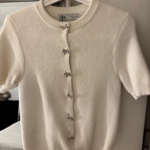 Vit kofta från Zara med rosettknappar - Supersöt vit kofta från Zara med korta ärmar och unika silvriga rosettformade knappar. De kommer inte till användning och används få gånger.
