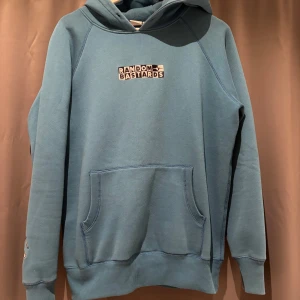 Blå hoodie från Random Bastards - Säljer en blå hoodie från Random Bastards med broderad logga på bröstet och en logga på ärmen.