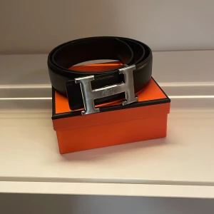 svart skärp med H-spänne - Säljer ett svart skärp. Bältet är tillverkat i exklusivt skinn och levereras i box. Perfekt accessoar för att lyfta din outfit. Storlek 