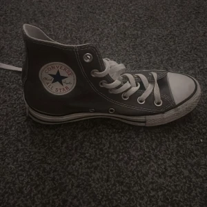 Svarta Converse All Star high-tops - Klassiska gråa Converse All Star high-tops med vit tå och vita snören. Skorna har rund tå, platt sula och tydliga vita sömmar. Ikonisk logga på sidan och slitstark canvas. Perfekta för en cool och avslappnad stil. Nästan helt nya bara använda några gånger