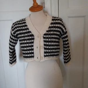 Randig croppad kofta i svart och vitt - Säljer en stickad, croppad kofta med svartvita ränder och breda ribbade kanter. Koftan har tre stora knappar framtill, lång ärm och en chunky känsla. Perfekt för dig som gillar retrovibbar och vill sticka ut lite extra.