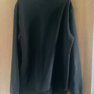 Svart sweatshirt från Man - Svart sweatshirt med broderad gul text 'Man' på bröstet. Tröjan har rund halsringning, långa ärmar och ribbade muddar vid ärmslut och nederkant. Perfekt för en chill och stilren look.