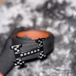 Svart skärp med H-spänne - Snyggt svart skärp  i präglat skinn med ikoniskt H-spänne i svart och vita detaljer. Insidan är brun och bältet har en exklusiv känsla som lyfter vilken outfit som helst. Perfekt accessoar för dig som gillar lyxiga detaljer.
