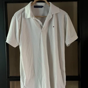 Vit pikétröja från Tommy Hilfiger - Vit pikétröja från Tommy Hilfiger med klassisk krage och två knappar framtill. Liten broderad logga på bröstet. Perfekt basic till garderoben och passar till det mesta.