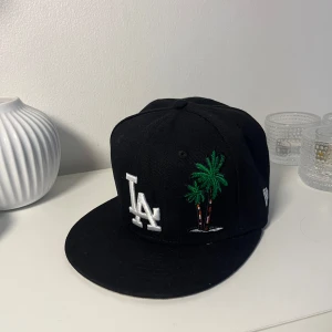 Svart LA Keps - Säljer en fet svart LA Keps med en snygg palmträd som design