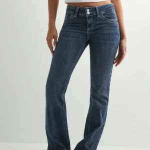 Nelly Blå bootcut jeans med broderade fickor - Snygga blå jeans med bootcut-modell och hög midja. Jeansen har klassisk femficksdesign och coola broderade detaljer på bakfickorna. Tillverkade i stretchig denim för skön passform och stilren look.