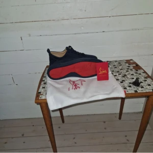 Christian Louboutin sneakers marinblå - Snygga marinblå sneakers från Christian Louboutin med den ikoniska röda sulan. Skorna har snörning och är tillverkade i mocka med läderdetaljer. Perfekta för dig som vill sticka ut med exklusiv stil och klassiska detaljer.