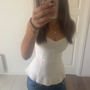 Vit korsettliknande topp med v-ringning - Säljer en snygg vit korsettinspirerad topp med v-ringning och figurnära passform. Toppen är ärmlös och har en utsvängd nederdel som ger en feminin siluett. Perfekt att styla med jeans eller kjol för en trendig look.