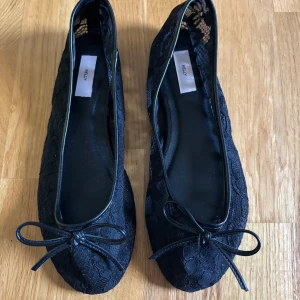 Svarta spetsballerinor - Snygga svarta ballerinaskor från Nelly med spetsdetaljer och liten rosett framtill. Skorna har rund tå och platt sula, vilket gör dem både stilrena och bekväma. Perfekta att matcha med både jeans och klänning för en trendig look. Endast använda en gång men säljer för att dom är för stora för mig. Dom är stora i storleken så passar dig som har 38/39 vanligtvis. Nypris 350kr