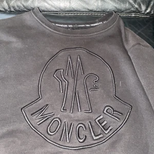 Svart Moncler sweatshirt med broderad logga - Svart moncler tröja limited eddition black on black Äkta, sweatshirt från Moncler Grenoble med stor broderad logga framtill. Tröjan har rund halsringning och är tillverkad i mjuk bomullsmix med 5% polyester. Perfekt för dig som gillar stilrena och exklusiva plagg. Lägg ett bud 