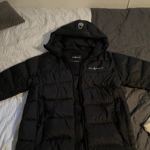 Sail Racing Jacka - Sail Racing JR Cloud Down Hood – Jackan har inga synliga spår av användning – ser i princip oanvänd ut. Lätt, varm och stilren dunjacka med huva, perfekt för höst och vinter. Klassisk Sail Racing-design med hög kvalitet och snygga detaljer.