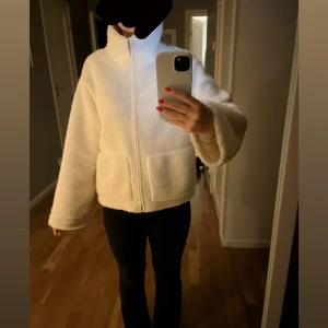 Vit teddyjacka med dragkedja - Mysig vit teddyjacka från Just Female med hög krage och dragkedja framtill. Jackan har två stora fickor och är tillverkad i fluffigt teddy-material. Perfekt för kyliga dagar och ger en trendig, avslappnad look.