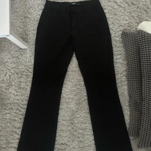 Svarta kostymbyxor med bootcut - Snygga svarta kostymbyxor med bootcut-snitt, låg midja och klassiska fickor både fram och bak. Byxorna har bälteshällor och är tillverkade i ett mjukt, välsittande material som ger en clean och stilren look. Perfekta för dig som gillar en tidlös och dressad stil. Från bik bok modell Vera i storlek 34. Använd 2-3 gånger så väldigt oanvända.