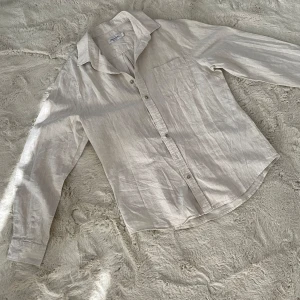 Ljusbeige linneskjorta Dressmann  - Snygg ljusbeige skjorta från Dressmann i linnemix, perfekt för dig som gillar en chill och stilren look. Skjortan har klassisk krage, bröstficka och knappar framtill. Långärmad och lätt material som känns fräscht under varma dagar.