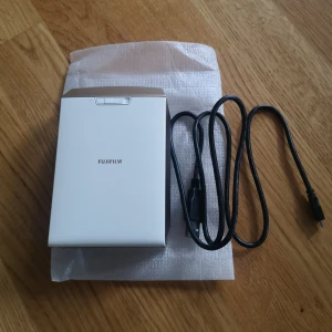 Instax Share SP-2 - Fujifilm Instax Share SP-2 mobil fotoskrivare som är sparsamt använd. Skriv ut bilder direkt från din smartphone via WiFi. Levereras UTAN instax mini films men den kommer med USB-laddkabel. Inga synliga repor eller skador och fungerar utmärkt. Perfekt för att skapa fysiska minnen snabbt och enkelt. Den har LED-indikator som visar hur många bilder det finns kvar också!