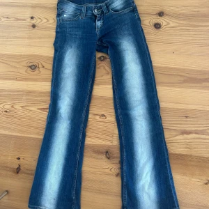 Blå bootcut jeans Cheap Monday - Snygga blå jeans från Cheap Monday med bootcut-modell och markerad ljus tvätt längs benen. Klassisk femficksdesign, normal midja och tydlig logga bak på linningen. Perfekta för dig som gillar en retro vibe och vill sticka ut lite extra.
