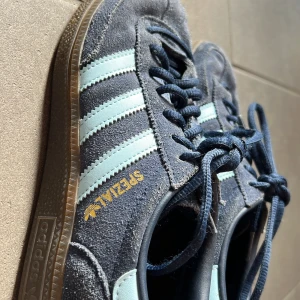 Adidas Spezial sneakers i blå mocka använda 5 ggr🩵💙 - Säljer ett par Adidas Spezial sneakers i blå mocka med ljusblå ränder och klassisk gummisula. Skorna har snörning och den ikoniska Adidas-loggan i guld på sidan. Insidan är mönstrad med Adidas-tryck. Perfekta för dig som gillar retrostil och streetwear.