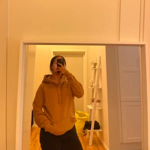 Gul hoodie med huva och ficka - Säljer en gul hoodie med huva och snörning. Tröjan har en stor magficka och en relaxed passform, perfekt för chill dagar. Mjuk insida och långa ärmar gör den extra bekväm.