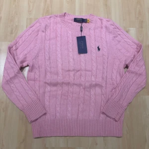 Rosa kabelstickad tröja Polo Ralph Lauren - Supersnygg rosa kabelstickad tröja från Polo Ralph Lauren. Klassisk rund halsringning, långärmad och med den ikoniska broderade loggan på bröstet. Perfekt för lager-på-lager och ger en fräsch vibe till din outfit.
