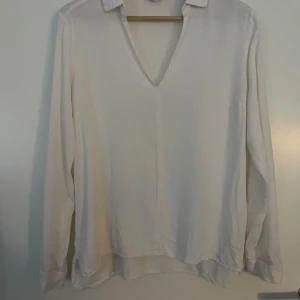 Vit v-ringad skjorta Bondelid M - Stilren vit skjorta från Bondelid i storlek M. Skjortan har v-ringning, klassisk krage och långa ärmar. Materialet känns mjukt och svalt, perfekt för en clean och enkel look. Broderad Bondelid-logga nertill på framsidan.