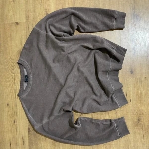 Brun basic tröja med rund hals - Enkel brun tröja med rund halsringning och långa ärmar. Tröjan har ribbade muddar vid ärmslut och nederkant, perfekt för lager-på-lager. Passar dig som gillar en clean och avslappnad stil.